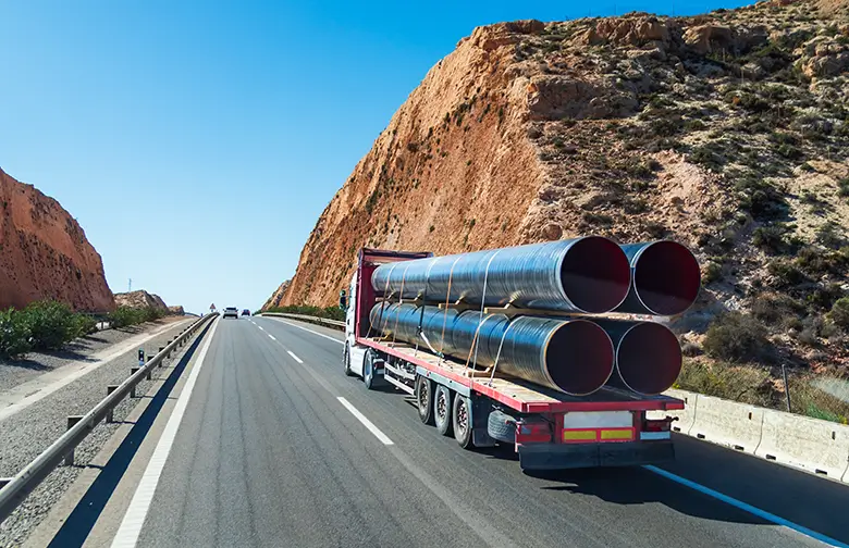 Truck transporting large fabricated metal pipes on a desert highway